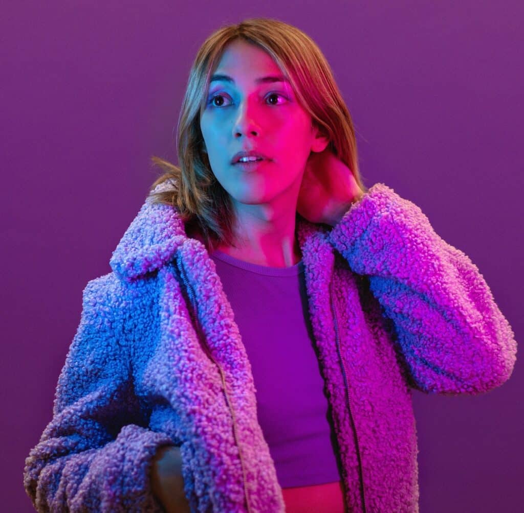 Alex Franklin is pictured in a purple coat with her arm behind her head, looking into the distance set against a purple background