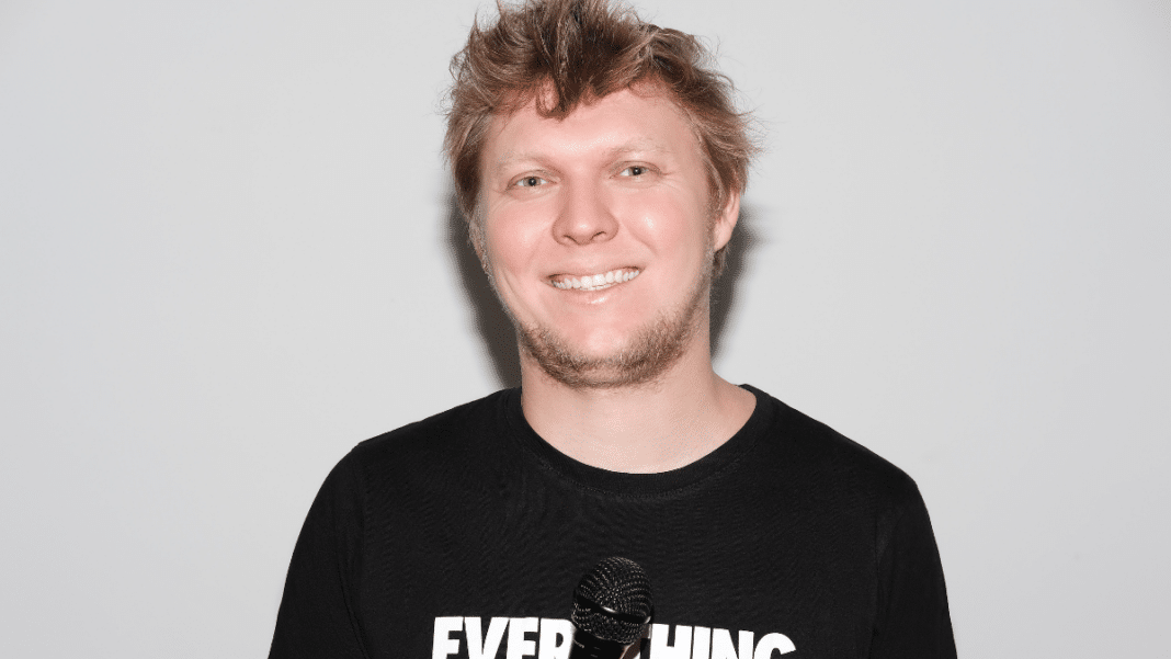 Stand up comedian Dima Watermelon is pictured smiling holding a microphone against a grey background