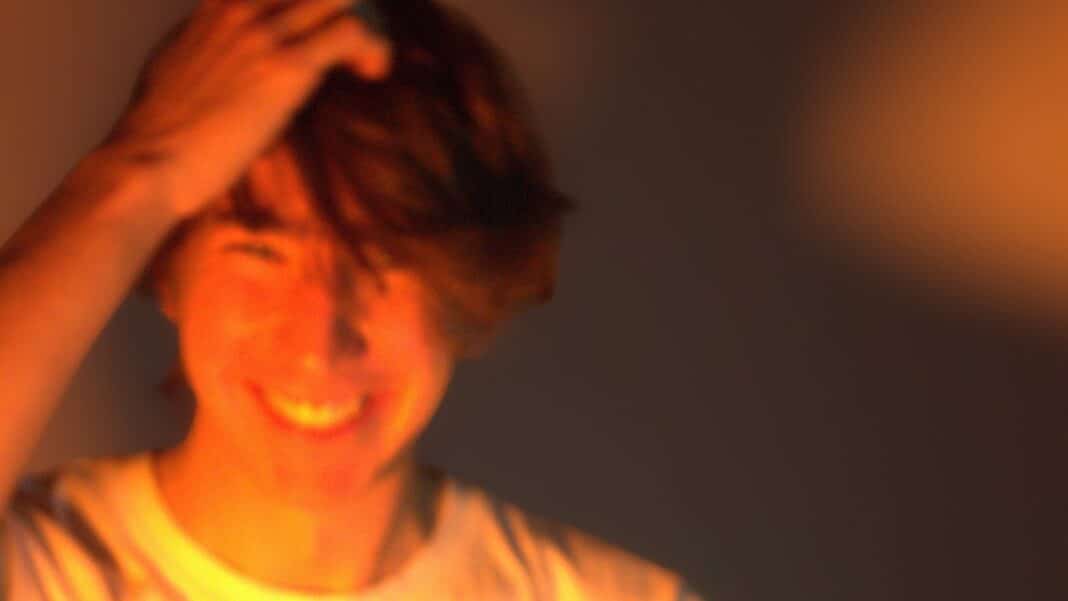 Charlie Prothero has an orange spotlight shining on him, the image is slightly out of focus and has a sense of movement