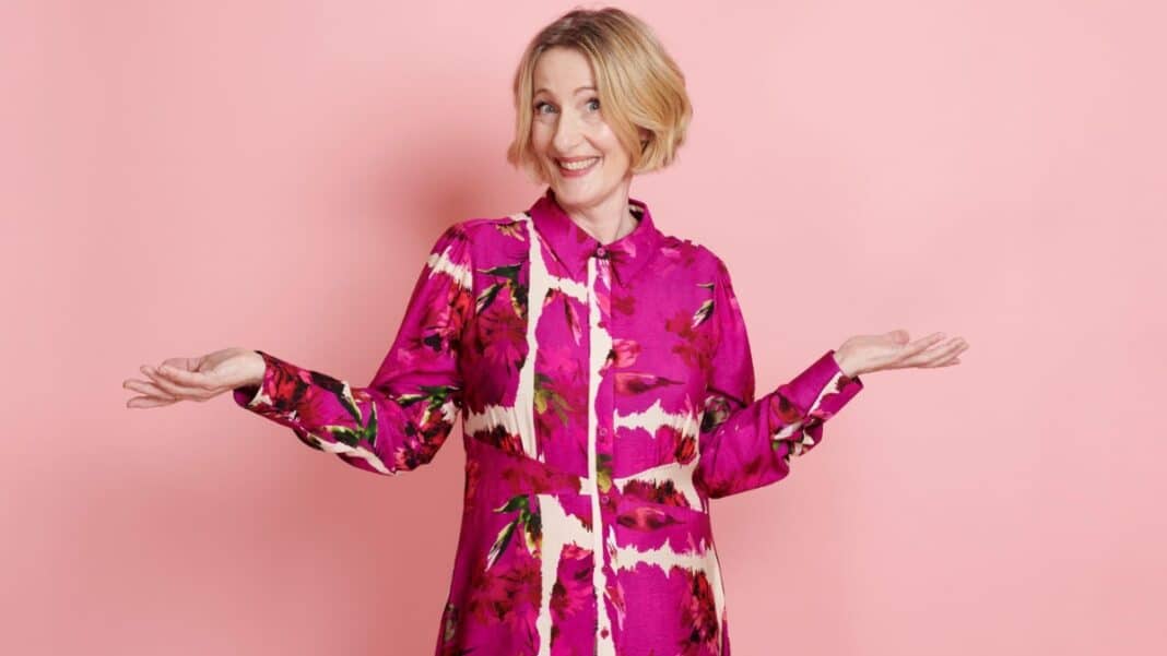 Sally Brockway in a vibrant pink dress with arms outstretched